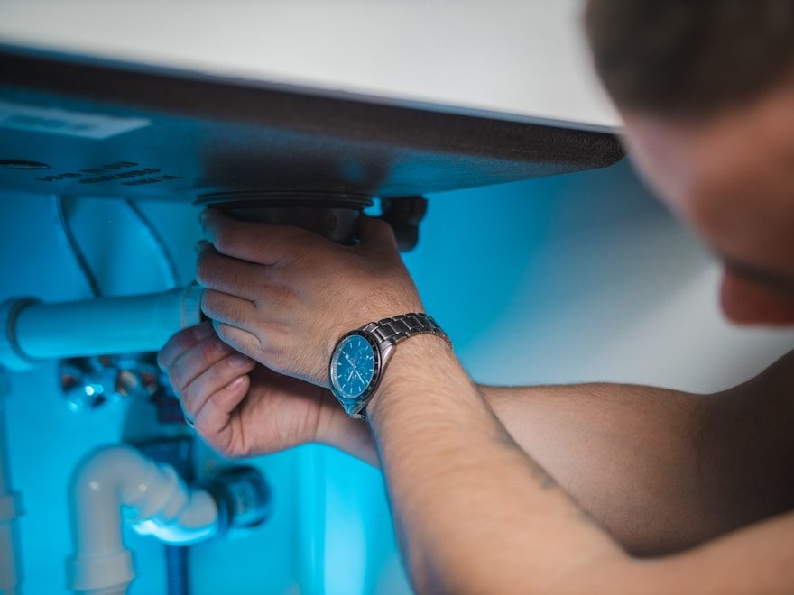 Plumber tightening a supply line under a sink
